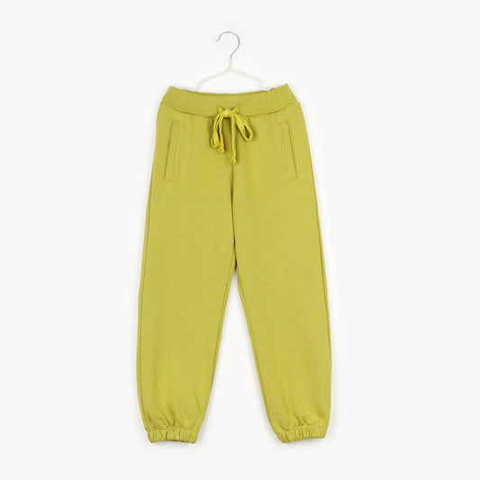 An image of a pair of acid green joggers, with a drawstring on the outside, two pockets on either side and cuffed hems hanging up on a white hanger against the background of a white wall.