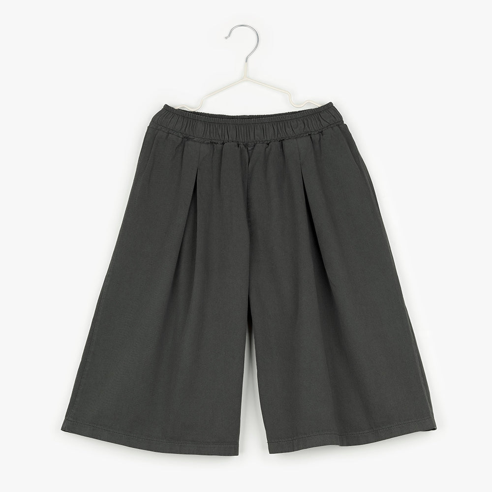 An image of grey, wide leg shorts hanging up on a white hanger against the background of a white wall. 