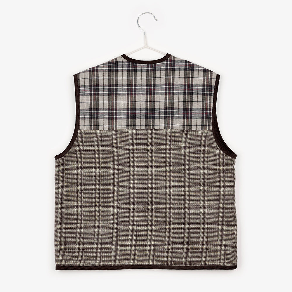 An image of the back of a gingham zip up vest hanging up on a white hanger against the background of a white wall.  The top of the vest is a tartan pattern, which contrasts with the 3/4 of the rest of the vest which is a brown checkered/gingham design. 