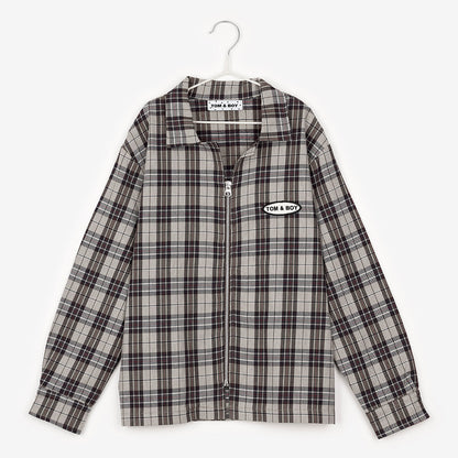 An image of a brown checkered/gingham zip up overshirt hanging up on a white hanger against the background of a white wall. To the right of the zipper it says Tom&Boy in black writing inside a white circle with a black border, similar to the design of a car mechanics work shirt.