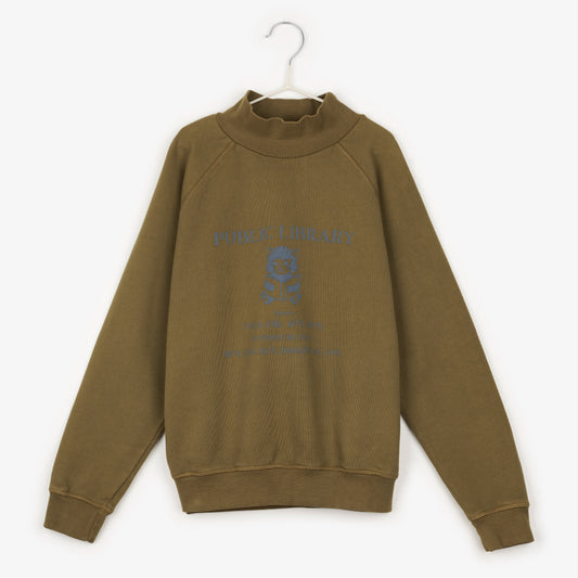 An image of a khaki high neck jumper that has the words public library in black. Beneath that is an image of a kitten reading a book, with the words 'Tues.-Fri. 1PM.4P,' underneath. Underneath that it says 'Summer-Fri. Only' and underneath that it says '100 N. Walnut. Broadway. Cos' hanging up on a white hanger against the background of a white wall.