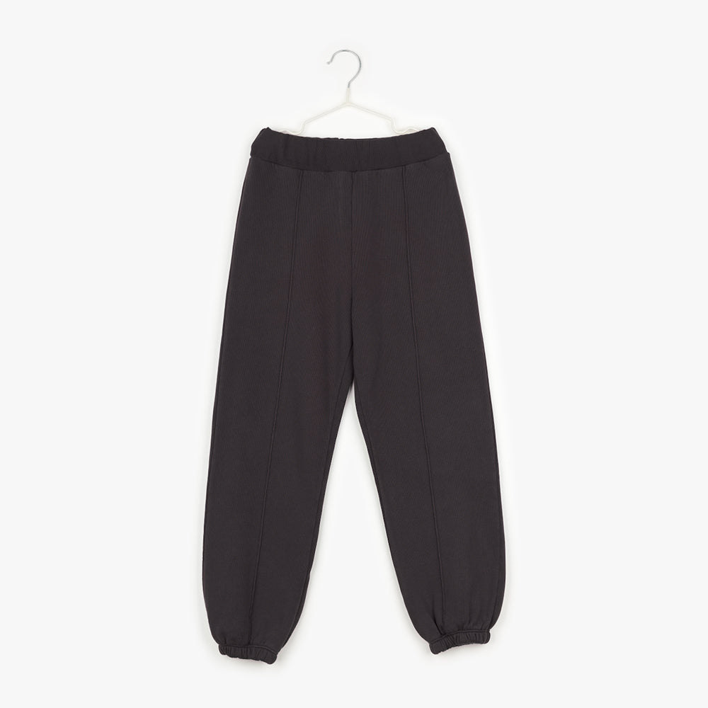 A pair of off-black trousers with an elasticated waist and cuffed hems. Down the front of the trouser is black piping. 