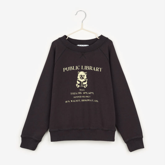 a black high neck jumper that has the words public library in off-white. Beneath that is an image of a kitten reading a book, with the words 'Tues.-Fri. 1PM.4P,' underneath. Underneath that it says 'Summer-Fri. Only' and underneath that it says '100 N. Walnut. Broadway. Cos' hanging up on a white hanger against the background of a white wall.