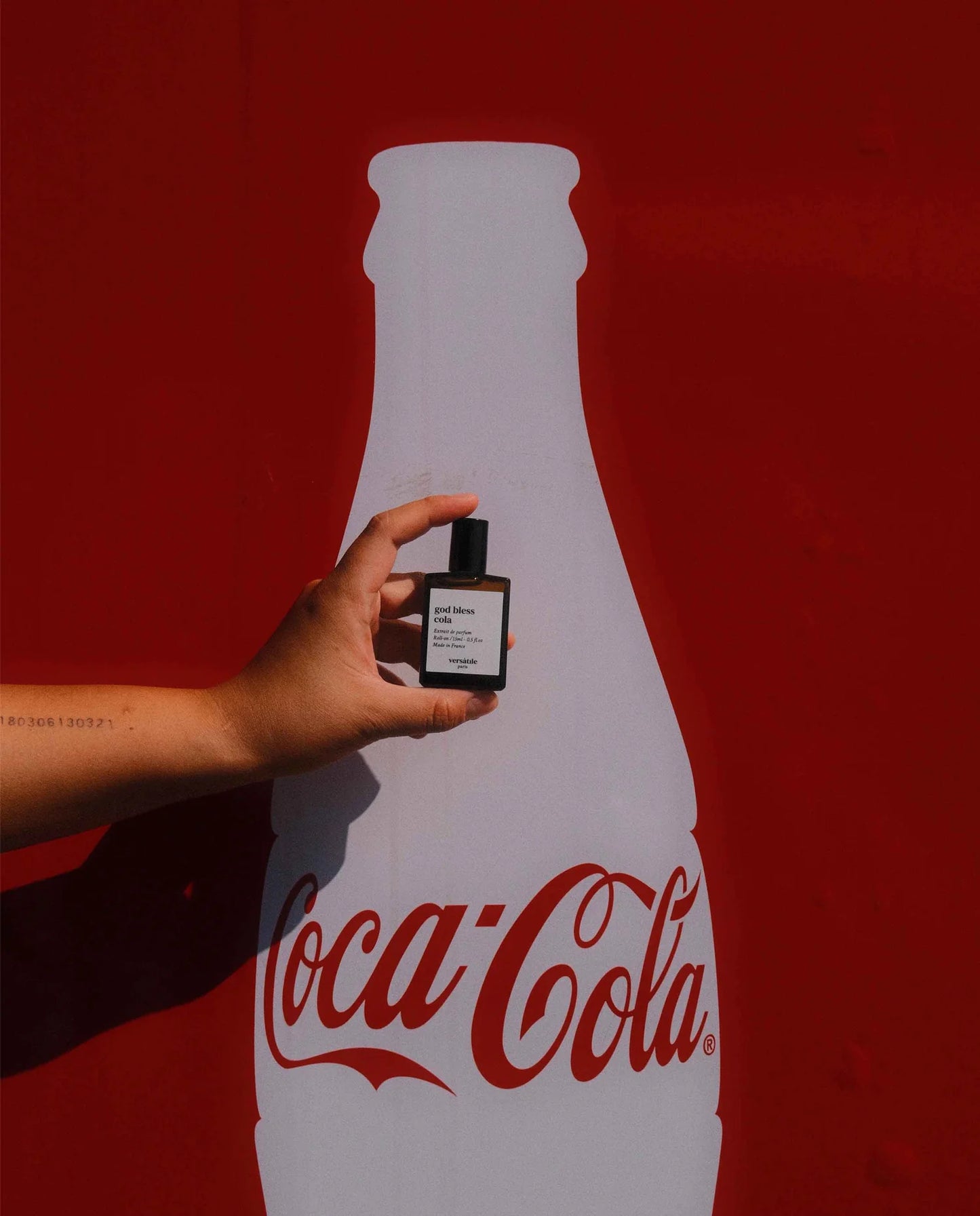Hand holding a small bottle in front of a large Coca-Cola bottle silhouette on a red background