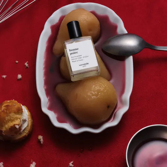 Perfume bottle labeled 'bonne poire' on a plate with pears on a red background