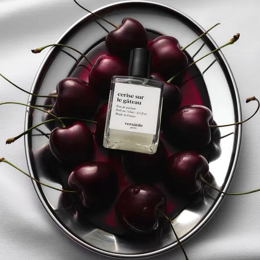Versace perfume bottle surrounded by cherries on a reflective surface