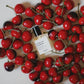 Versace perfume bottle surrounded by red cherries on a light background