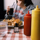 Person sitting at a table with food and condiments, wearing a 'Washington DC' sweatshirt.