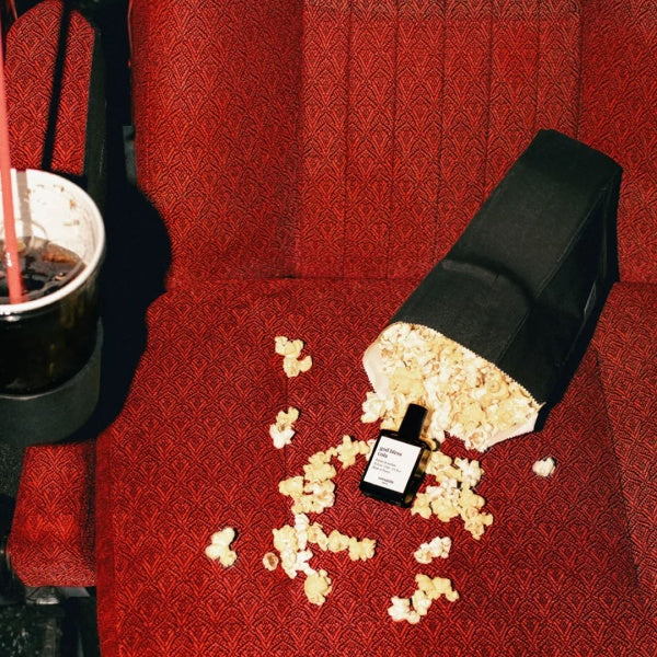 Popcorn and a bottle on a red movie theater seat with a cup of soda.