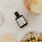 Perfume bottle labeled 'sea salt & sun' on a marble surface with olives and glasses.