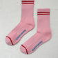 A pair of Le bon shoppe amour pink boyfriend socks which are pink in colour with red stripes at the top and near the toes.It says Le Bon shoppe on the sole of the socks in blue colour. The socks are kept against a white background. 