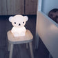 A glowing Boris First Light Lamp sits on a wooden stool beside a sleeping baby in a dimly lit nursery.