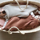 Two babies in an orange and off white wool cocoons placed in a rope basket on a wooden panel floor.
