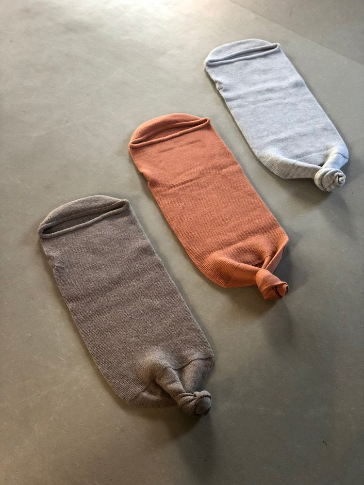 Brown, orange and off white wool baby cocoons placed on a beige background.