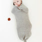 Baby inside a grey melange wool cocoon lying on a white background.