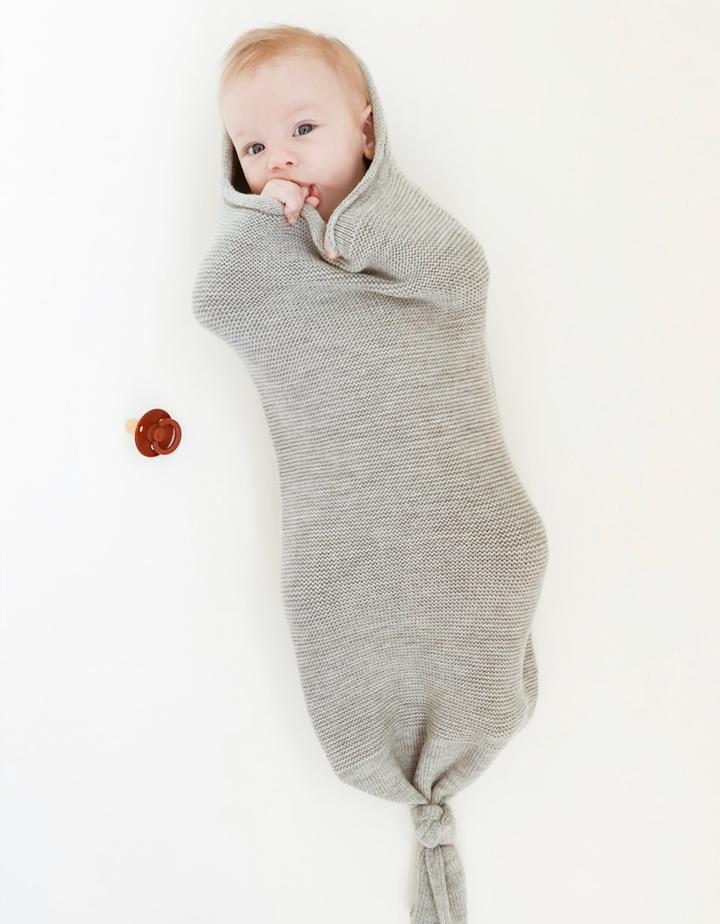 Baby inside a grey melange wool cocoon lying on a white background.