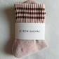 A pair of Bellini pink ribbed crew socks with brown multi-stripe details, neatly folded and wrapped with a white Le Bon Shoppe label, placed on a white fabric background.