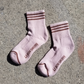 A close-up of Bellini pink ribbed crew socks with brown stripes, showing the thick ribbed texture, cushioned heel, and Le Bon Shoppe branding on the sole.