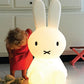 Mr Maria Miffy XL Lamp, 80 cm tall, iconic statement piece with six brightness settings, inspired by Dick Bruna's classic illustrations. It is lit up and small toddler in e red dress stands next to it for scale