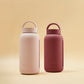 A matte Silicone covered glass bottle, with a window to see the drink on the inside, in a deep Plum Purple colour with a plastic screw top circular lid with a handle