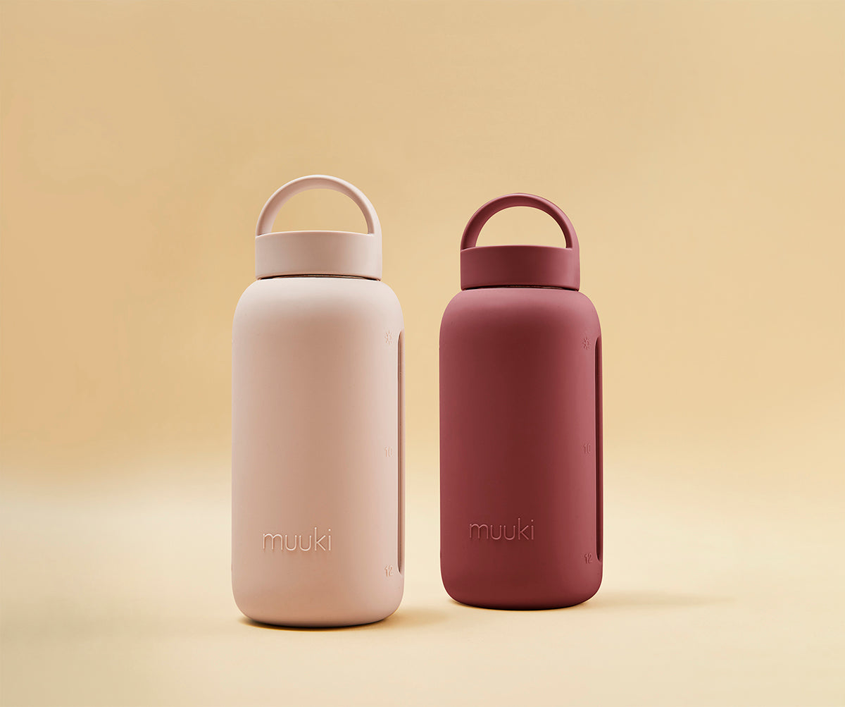 A matte Silicone covered glass bottle, with a window to see the drink on the inside, in a deep Plum Purple colour with a plastic screw top circular lid with a handle