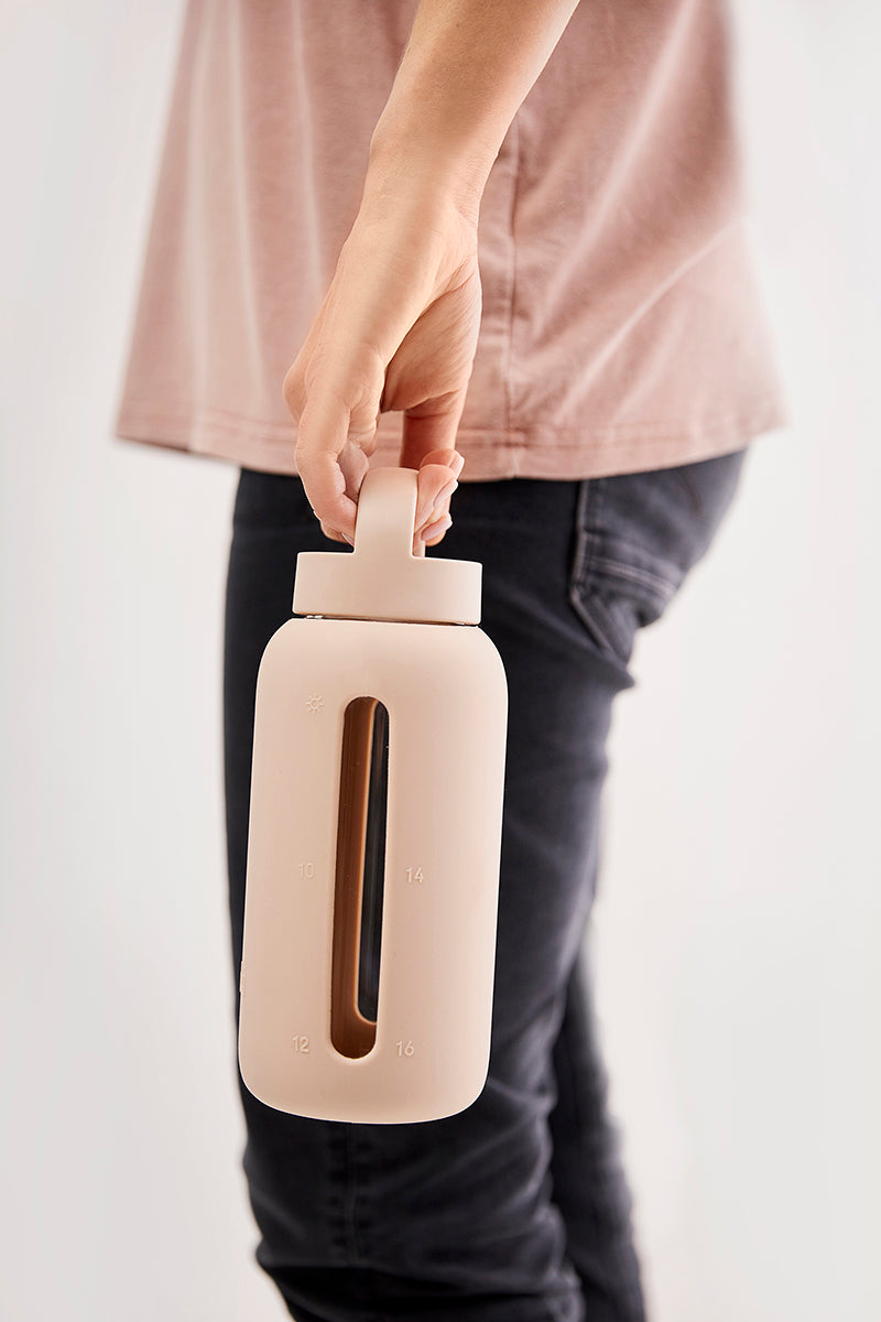 A matte Silicone covered glass bottle, with a window to see the drink on the inside, in a pinky cream colour with a plastic screw top circular lid with a handle