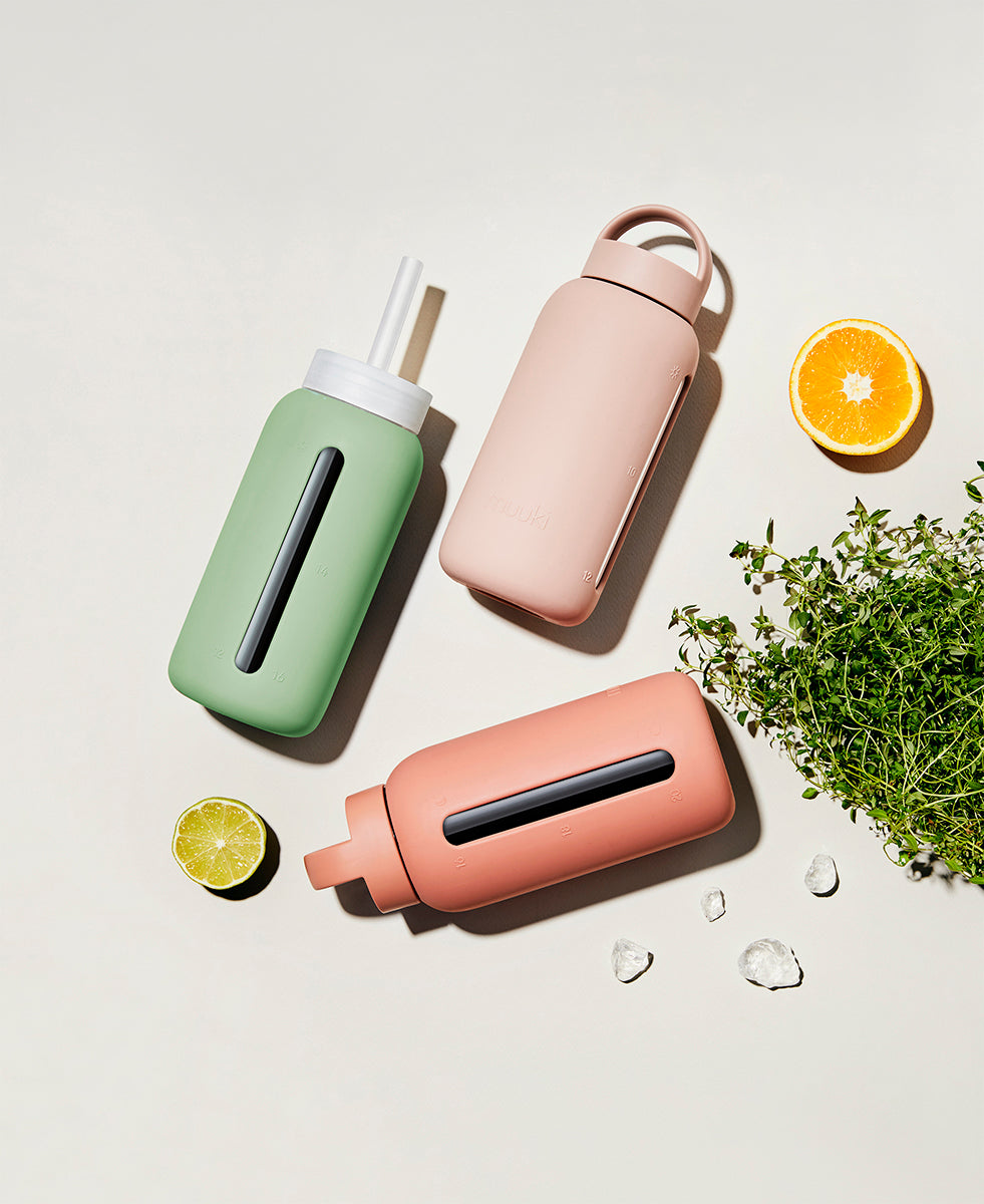 A matte Silicone covered glass bottle, with a window to see the drink on the inside, in a muted sage green colour with a plastic screw top circular lid with a handle