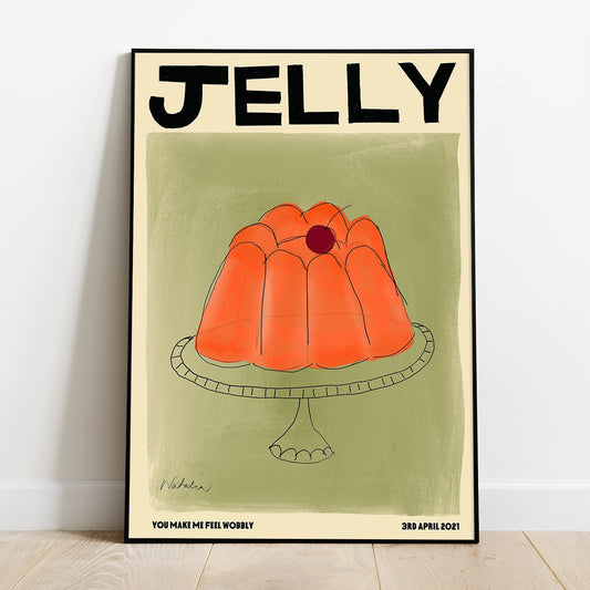 A Natalia Bagniewska jelly print that features an orange jelly with a red cherry on top. The jelly is on a glass transparent plate. The background is green. Beneath the green background it says You Make Me Feel Wobbly, in black, on the left hand side, and on the right hand side it says 3rd April 2021. The print is framed and kept against a white wall on a wooden floor. 