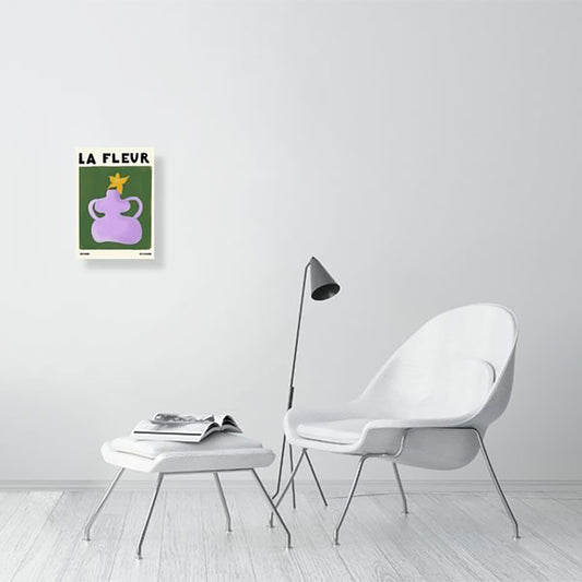 A Natalia Bagniewska La Fleur Print in a drawing room setting.The print features a background which is green. The flower pot is lilac and the flower is yellow. It say “la Fleur” which means the flower is French. The wall, chair, stool are all white with a white wooden floor. 