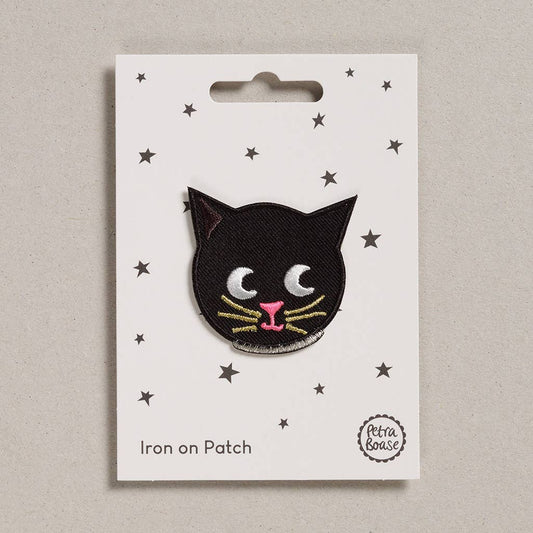 an embroidered cat face which is black in colour with a pink nose and mouth.The whiskers are golden and the eyes are black. The cat has a silver collar around its neck.The background is white with black stars.