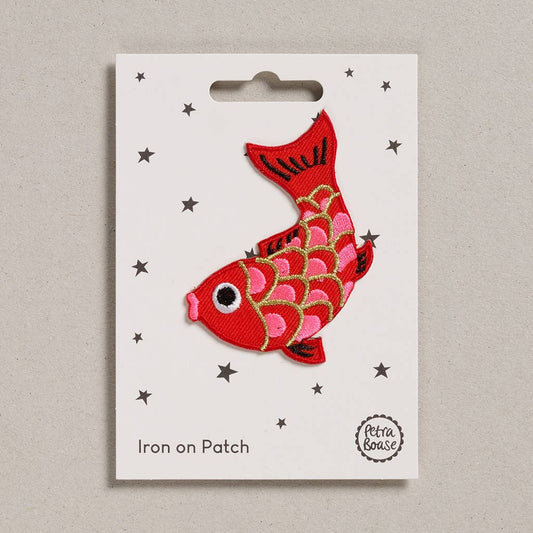 an embroidered koi fish. It is a red fish with pink scales lined with golden colour. The mouth is pink and it has black eyes . The background is white with black stars. 