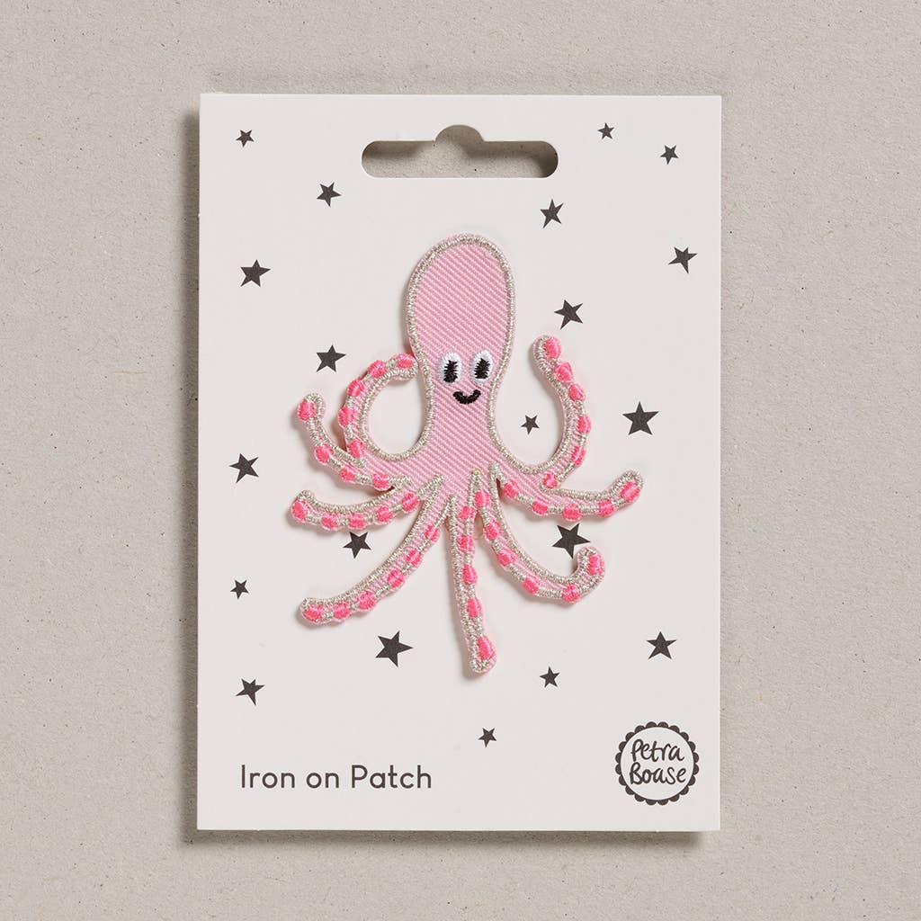 an embroidered pink octopus with dark pink tentacles. It has black eyes and a silver lining. The background is white with black stars