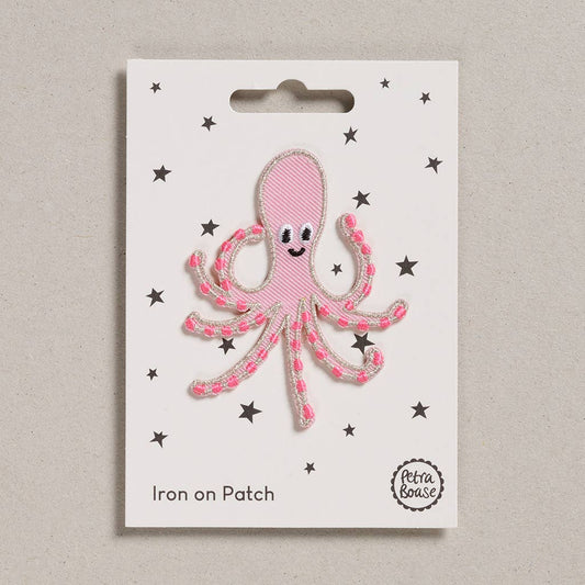 an embroidered pink octopus with dark pink tentacles. It has black eyes and a silver lining. The background is white with black stars