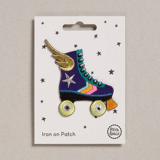 an embroidered purple rollerskate. It has a golden wing with yellow wheels. Its break is orange in colour. It has silver laces and a silver star. The stripes are green, orange and pink in colour. The background is white with black stars 