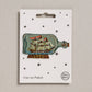 An embroidered iron-on patch featuring a classic tall ship with red sails inside a glass bottle, resting on a wooden stand with "Hope" stitched in gold. Packaged on a cream backing card with black stars and Petra Boase branding.