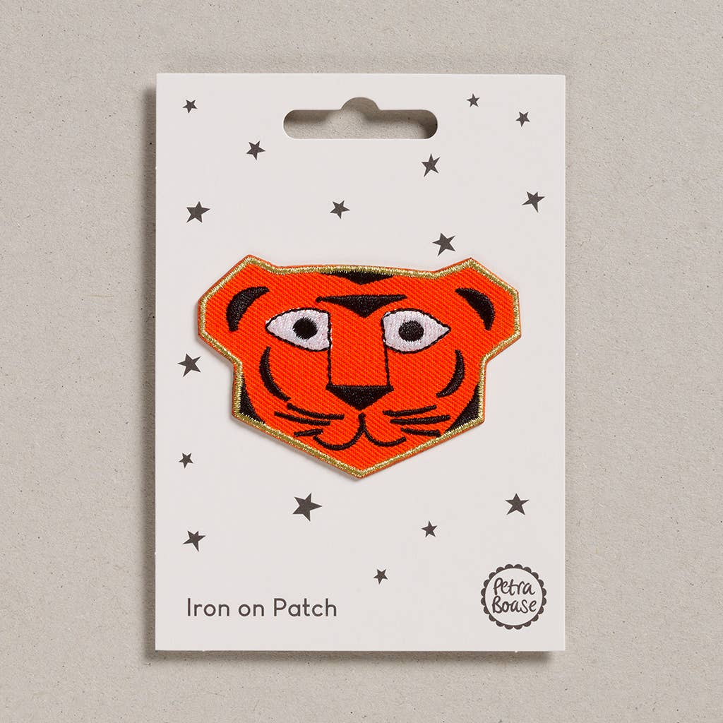 An embroidered orange tiger face. It has black stripes, nose, whiskers. The background is white with black stars
