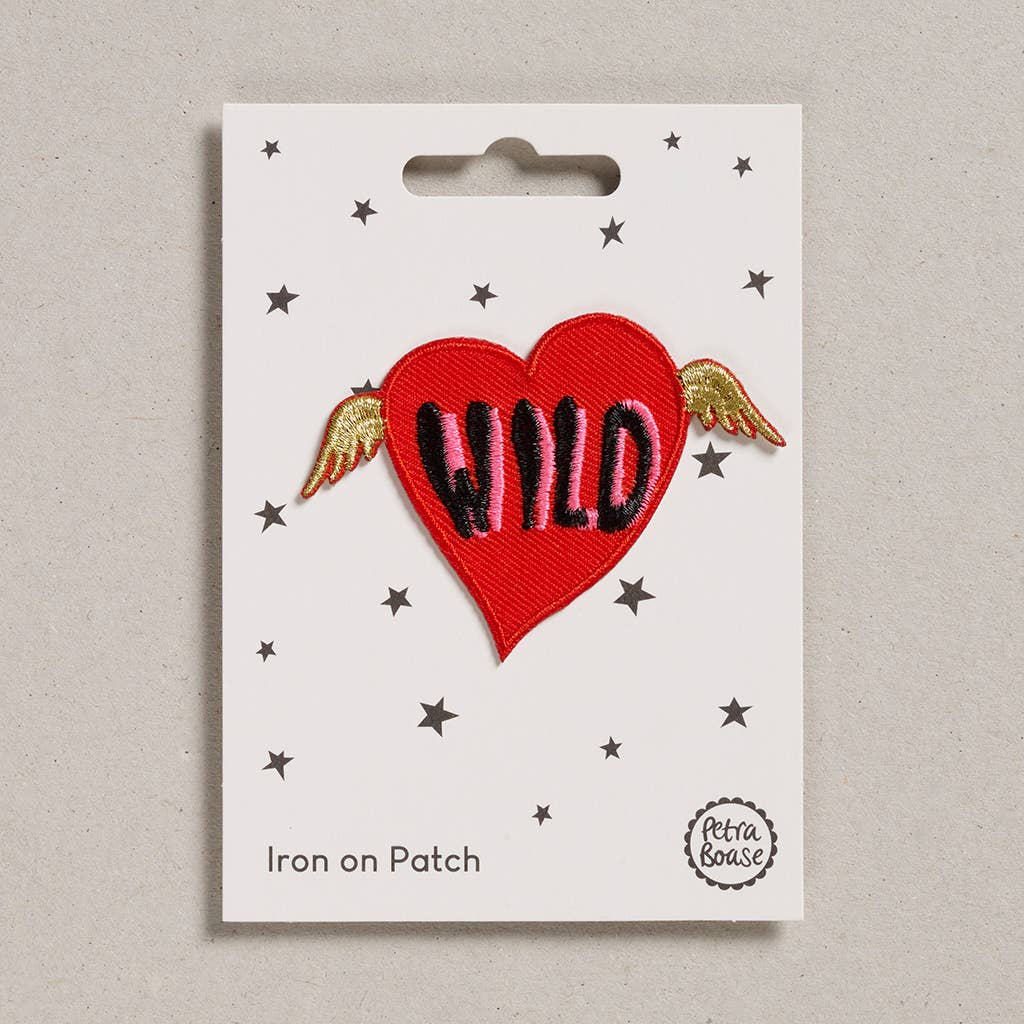 an embroidered red heart that has wild written on it with black and pink. The heart has golden wings. The background is white with black stars. 