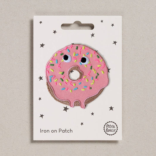  a doughnut with pink icing. It has googly eyes with sprinkles that are blue, pink, yellow. The background is white with black stars. 