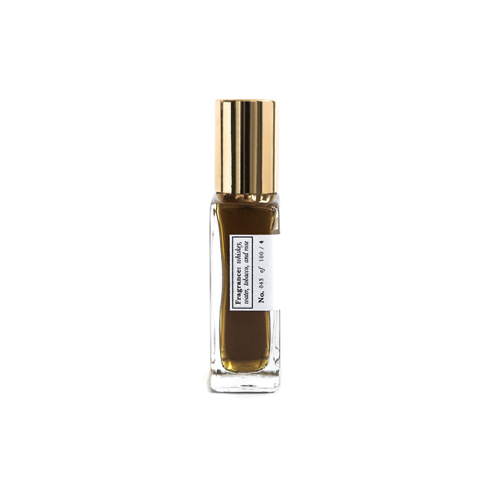 A glass bottle with a gold lid. The label is white with black text. The perfume is a dark gold colour. The bottle is shown from the side