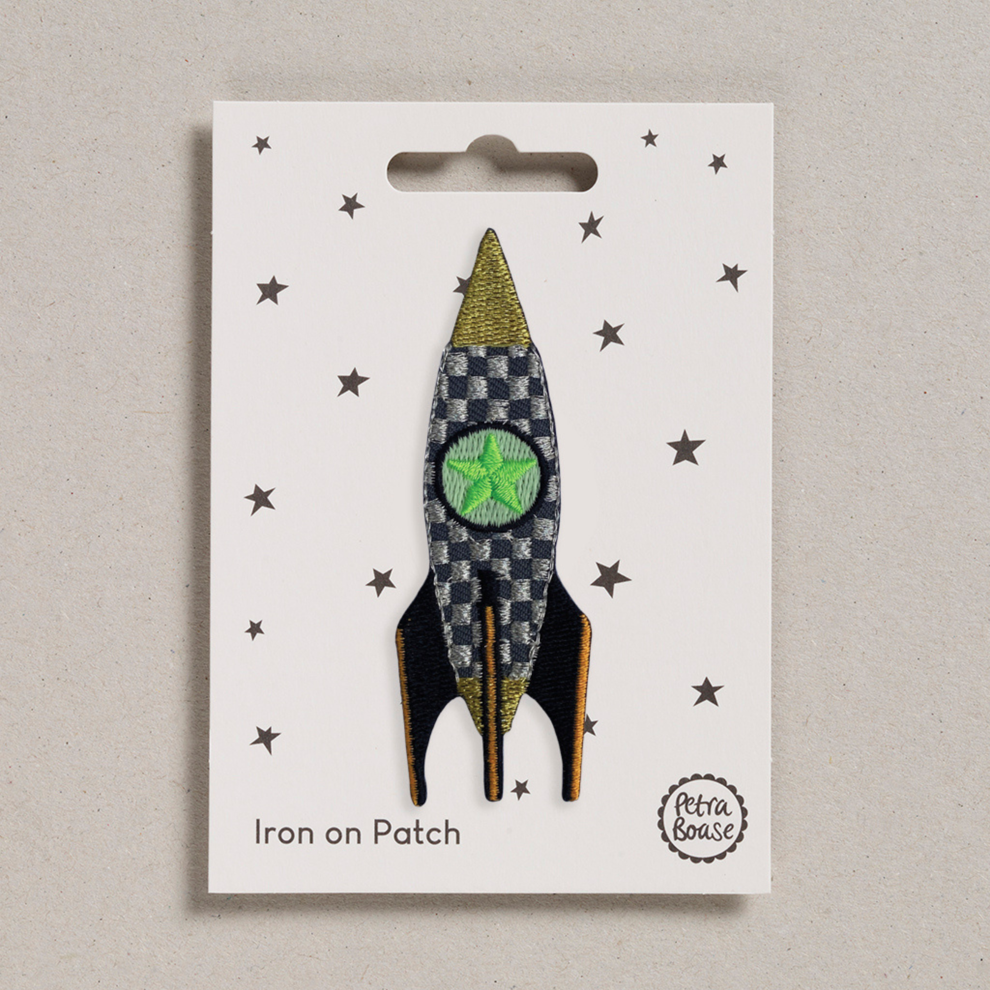 an embroidered rocket which has a dark and light grey checkered pattern with black wings and orange lines on them. There is a green star in the middle. The background is white with black stars. 
